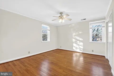 an empty room with wooden floor chandelier fan and windows