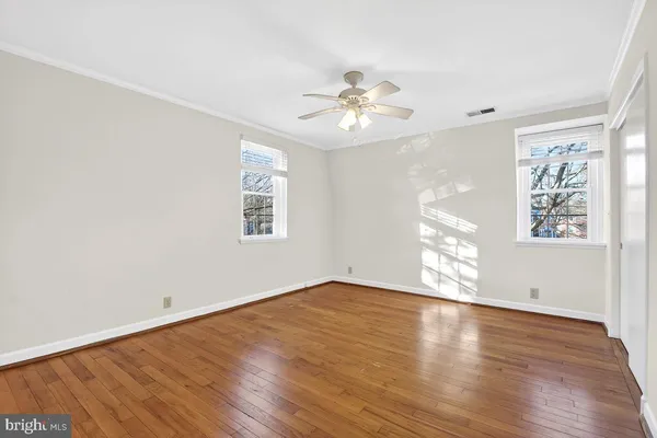 an empty room with wooden floor chandelier fan and windows