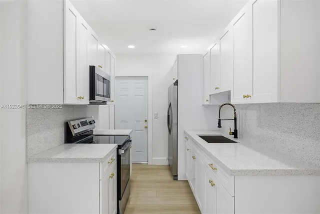 a kitchen with stainless steel appliances a sink a stove a refrigerator a white counter top and white cabinets