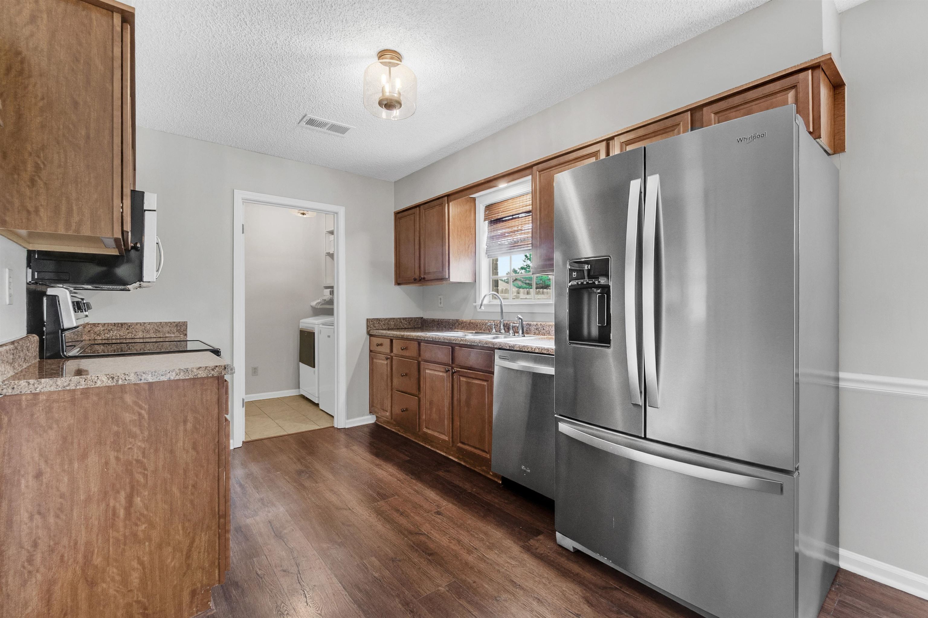 7255 Barnstable Road Memphis, TN 38125 - Photo 10 of 27 Kitchen featuring stainless steel appliances, brown cabinetry, baseboards, dark wood-style floors, and a textured ceiling