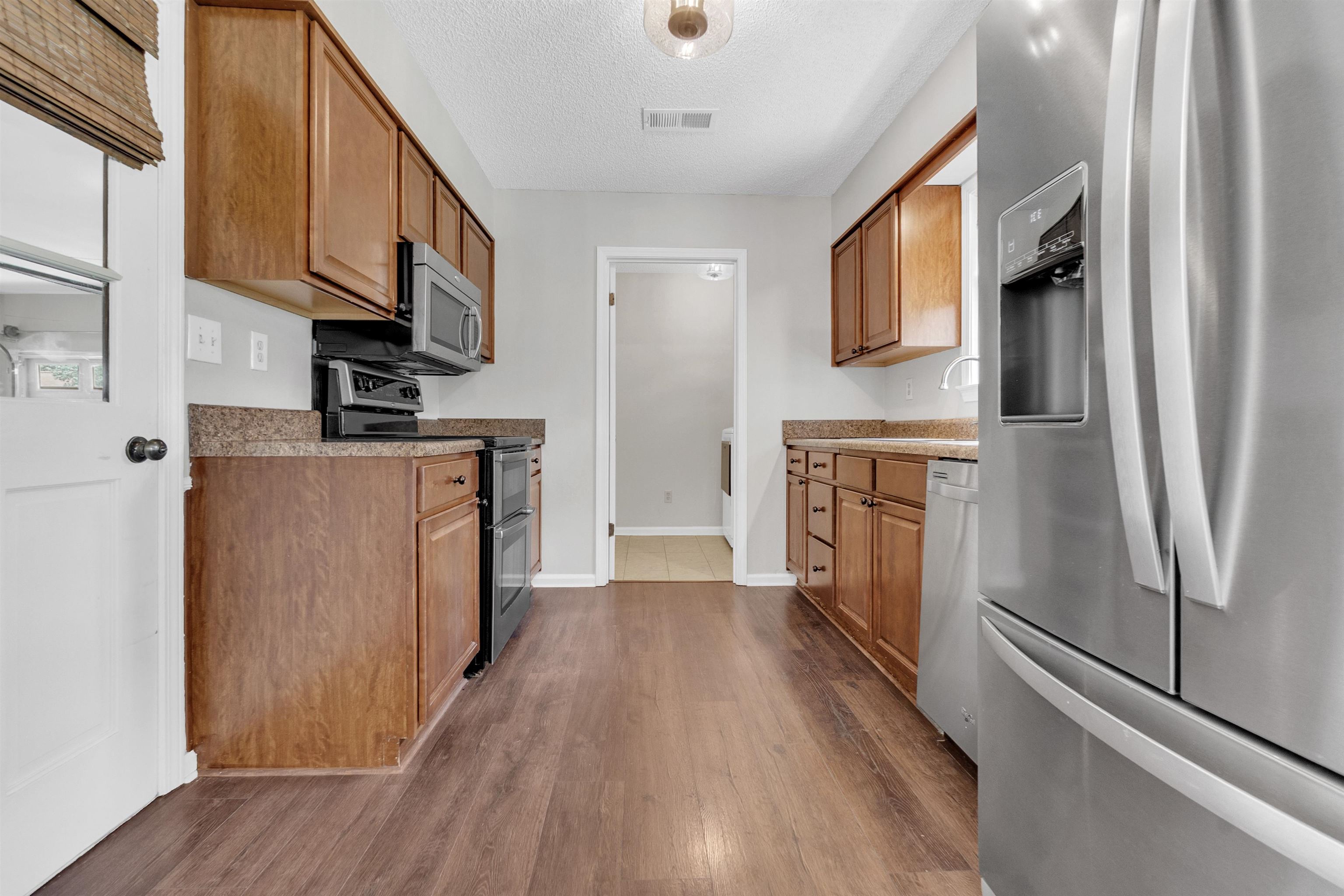 7255 Barnstable Road Memphis, TN 38125 - Photo 11 of 27 Kitchen with appliances with stainless steel finishes, dark wood-type flooring, brown cabinetry, a textured ceiling, and baseboards
