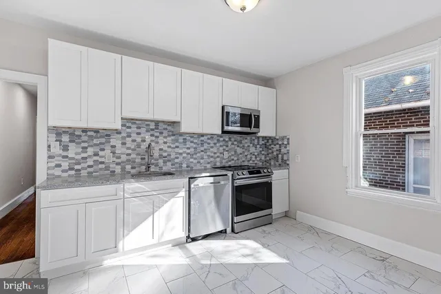 a kitchen with granite countertop white cabinets stainless steel appliances a sink and a window