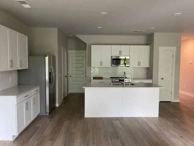 a large kitchen with stainless steel appliances a refrigerator a stove top oven a sink and dishwasher with wooden floor