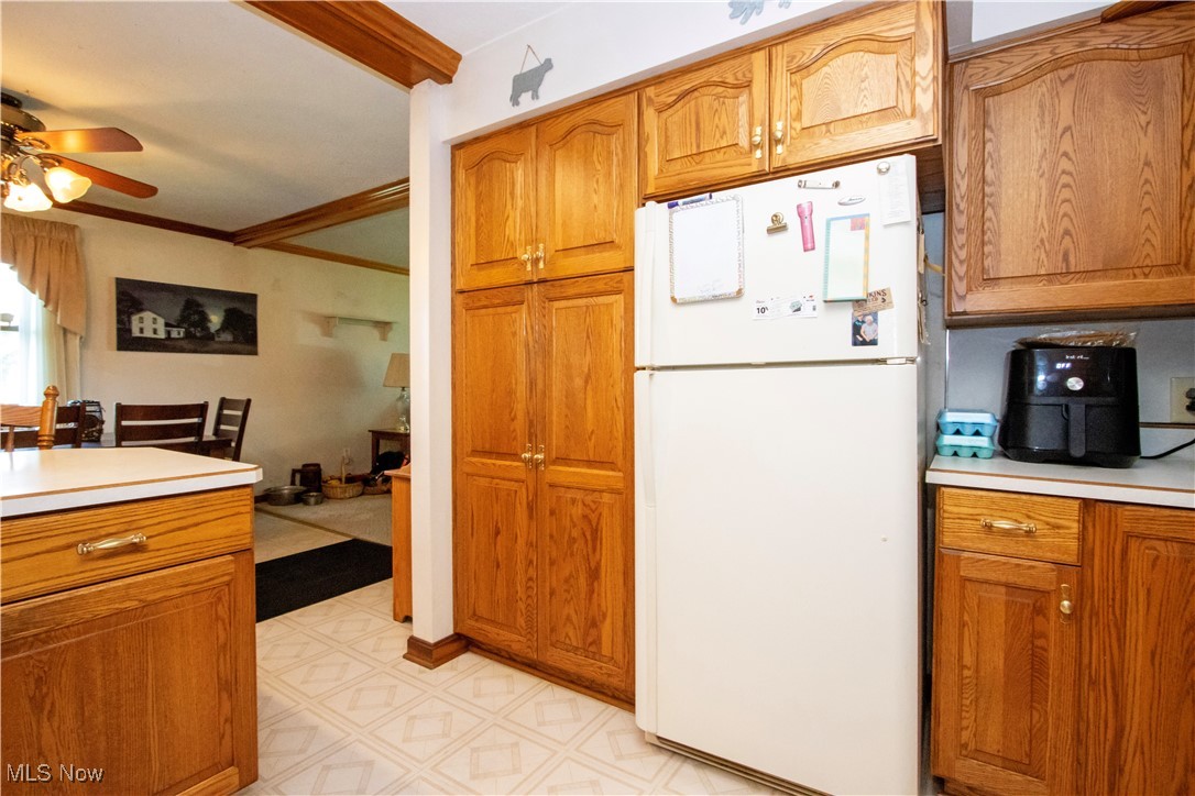 1292 Cinder Road Southeast Carrollton, OH 44615 - Photo 26 of 42 Kitchen featuring freestanding refrigerator, a ceiling fan, crown molding, light countertops, and brown cabinetry