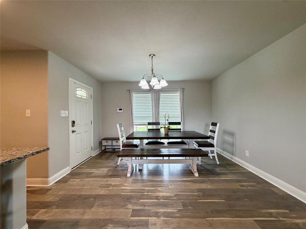 619 Mansfield Road Cleburne, TX 76031 - Photo 4 of 19 Open-concept dining area featuring wood-finish flooring, a contemporary chandelier, and a white paneled entry door with an arched glass insert