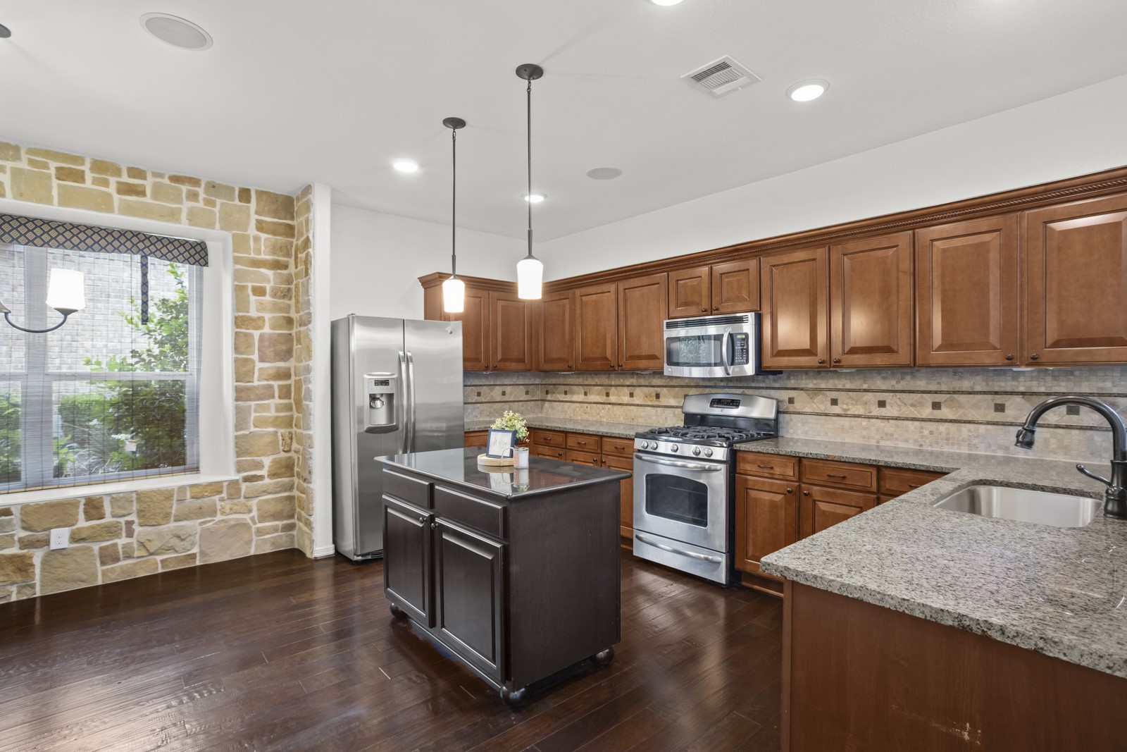 245 Razzmatazz Trail Buda, TX 78610 - Photo 10 of 37 Kitchen featuring a stone accent wall, dark wood-finish flooring, stainless steel appliances, granite countertops, and wood cabinetry