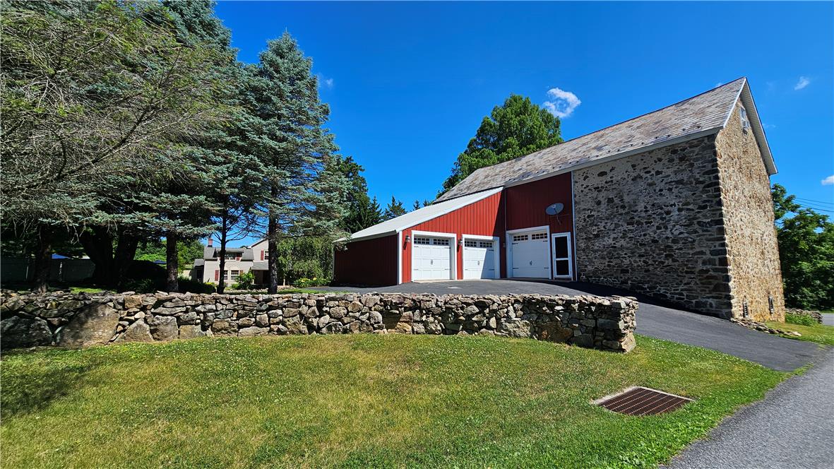 585 Buttermilk Road Hellertown, PA 18055 - Photo 66 of 82 A striking stone and red-sided barn with multiple garage doors sits beside a charming stone wall.