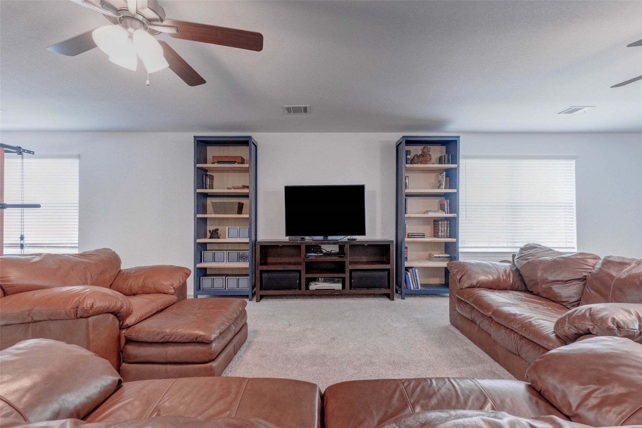 32418 Fly Fish Way Fulshear, TX 77441 - Photo 25 of 40 Flanked by two windows that fill the room with natural light, the game room features a generous media wall perfectly sized for a large screen television and entertainment setup, making this space an ideal destination for movie nights, gaming, or relaxing with family.