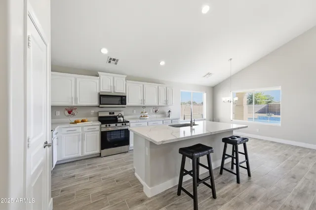 a kitchen with stainless steel appliances a stove a sink a refrigerator white cabinets and wooden floor