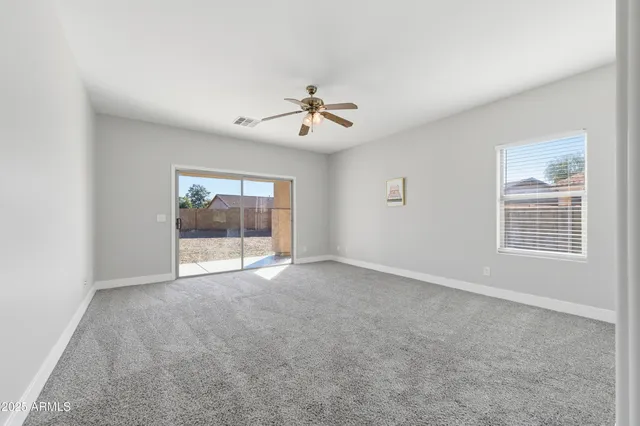 an empty room with chandelier fan and windows