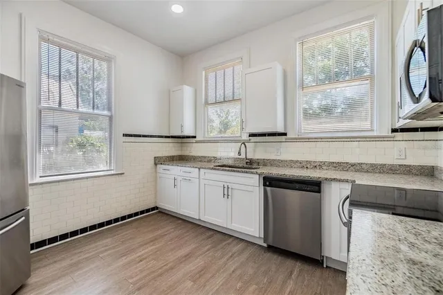 a kitchen with granite countertop wooden floors white cabinets a sink a window and appliances