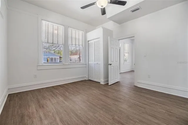 an empty room with wooden floor chandelier fan and windows