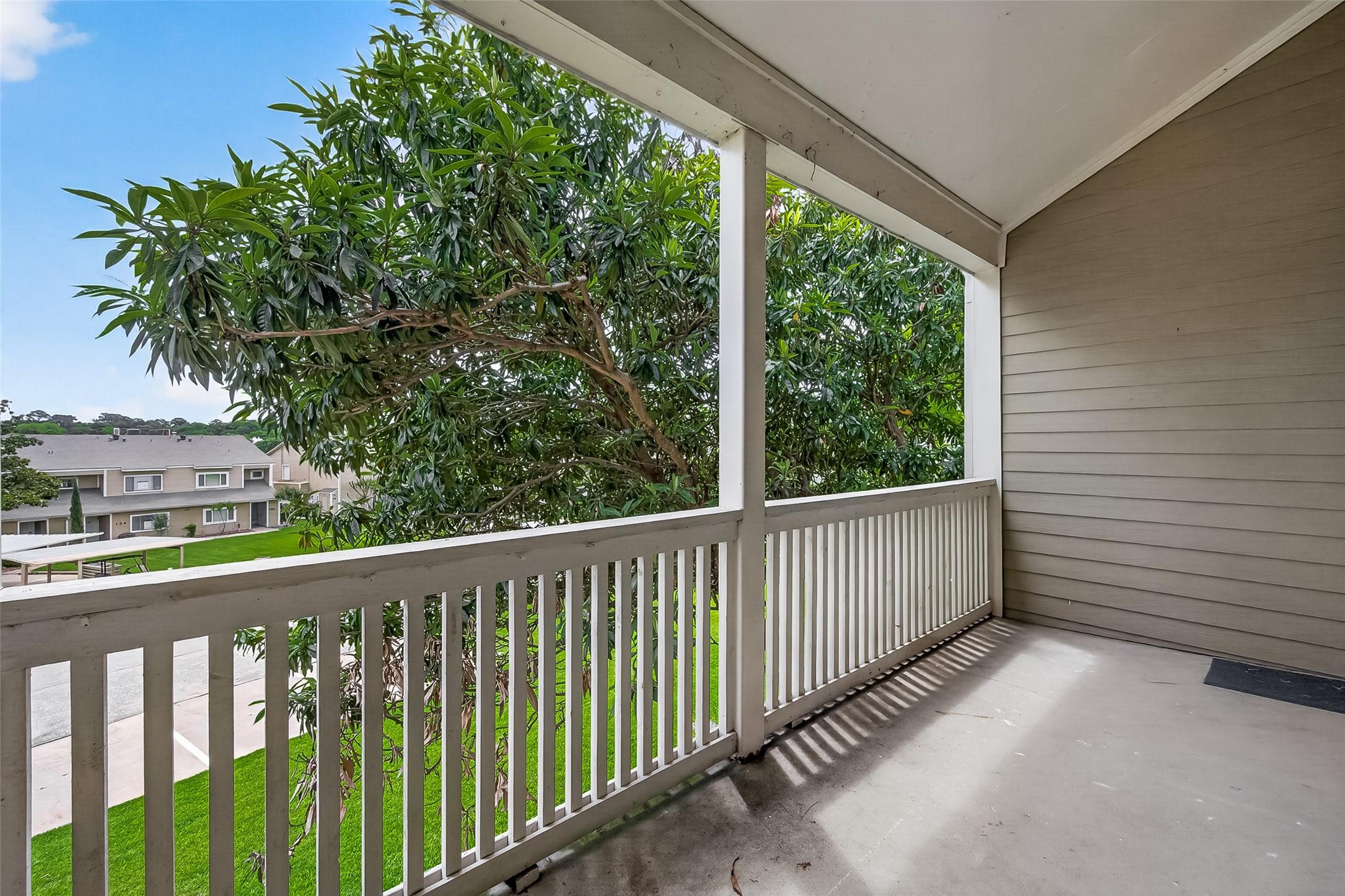 180 April Point Drive South Conroe, TX 77356 - Photo 12 of 39 This photo showcases a spacious covered balcony with a wooden railing, offering a view of nearby greenery and neighboring homes. Ideal for relaxation and enjoying the outdoors.