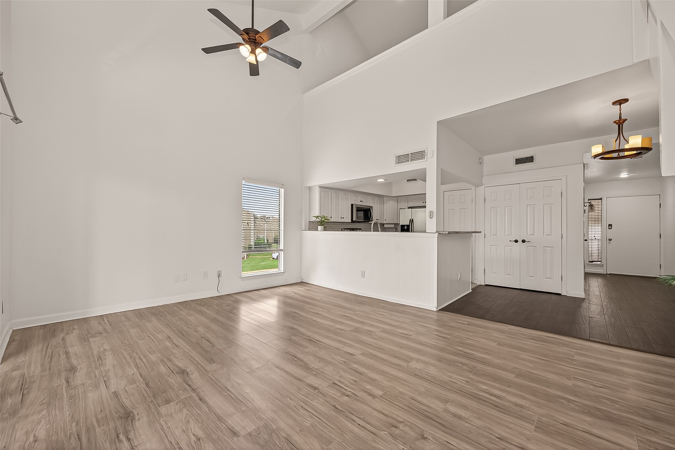 180 April Point Drive South Conroe, TX 77356 - Photo 13 of 39 This bright, open-concept living space features high ceilings, a modern ceiling fan, and laminate wood flooring. The kitchen, visible from the living area, includes sleek cabinetry and stainless steel appliances. Large windows offer ample natural light, and the space flows seamlessly into adjacent rooms, creating an inviting atmosphere.