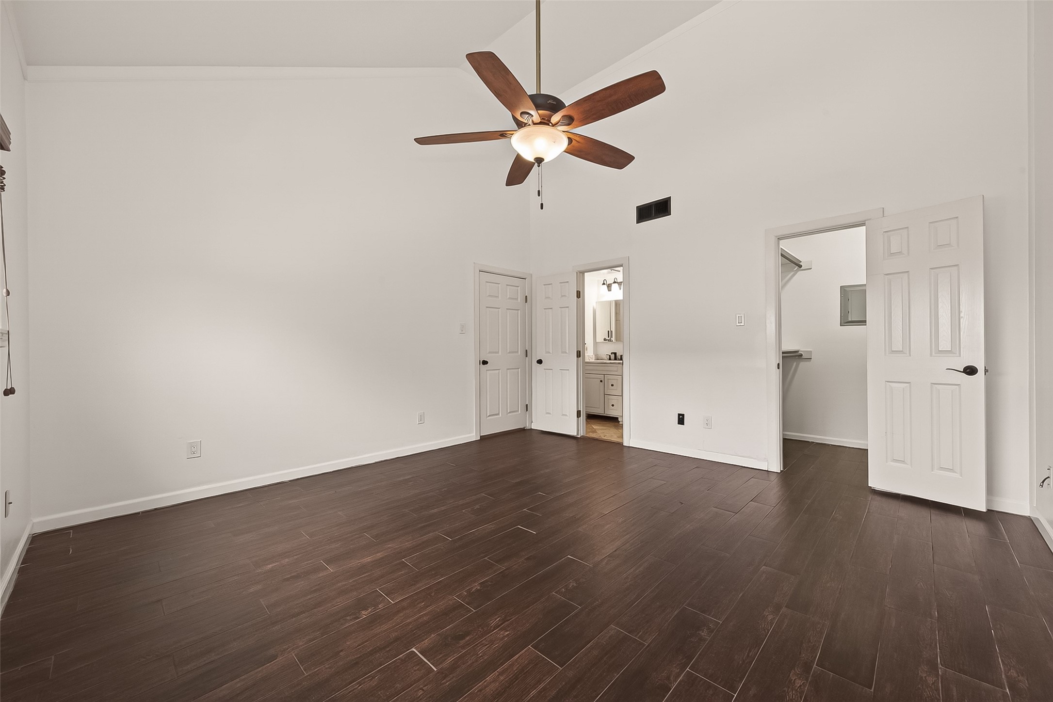 180 April Point Drive South Conroe, TX 77356 - Photo 14 of 39 This spacious primary room features dark wood flooring, high ceilings with a ceiling fan, and neutral walls. It includes access to a bathroom and a walk-in closet, providing convenience and functionality.
