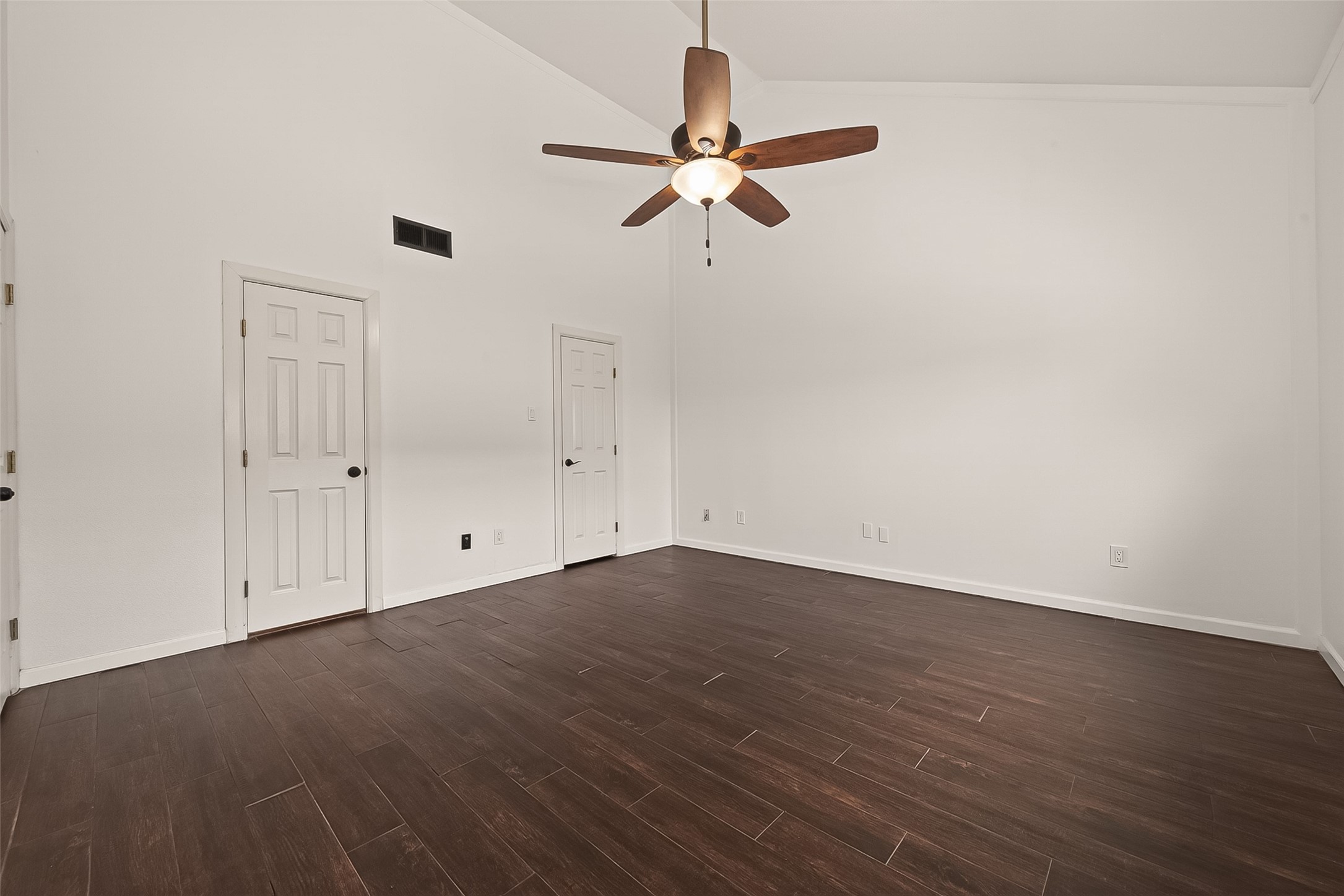180 April Point Drive South Conroe, TX 77356 - Photo 15 of 39 This primary room features high ceilings with a ceiling fan, sleek dark wood flooring, and a clean, minimalist design. It has two doors and neutral white walls, offering a spacious and versatile living area.