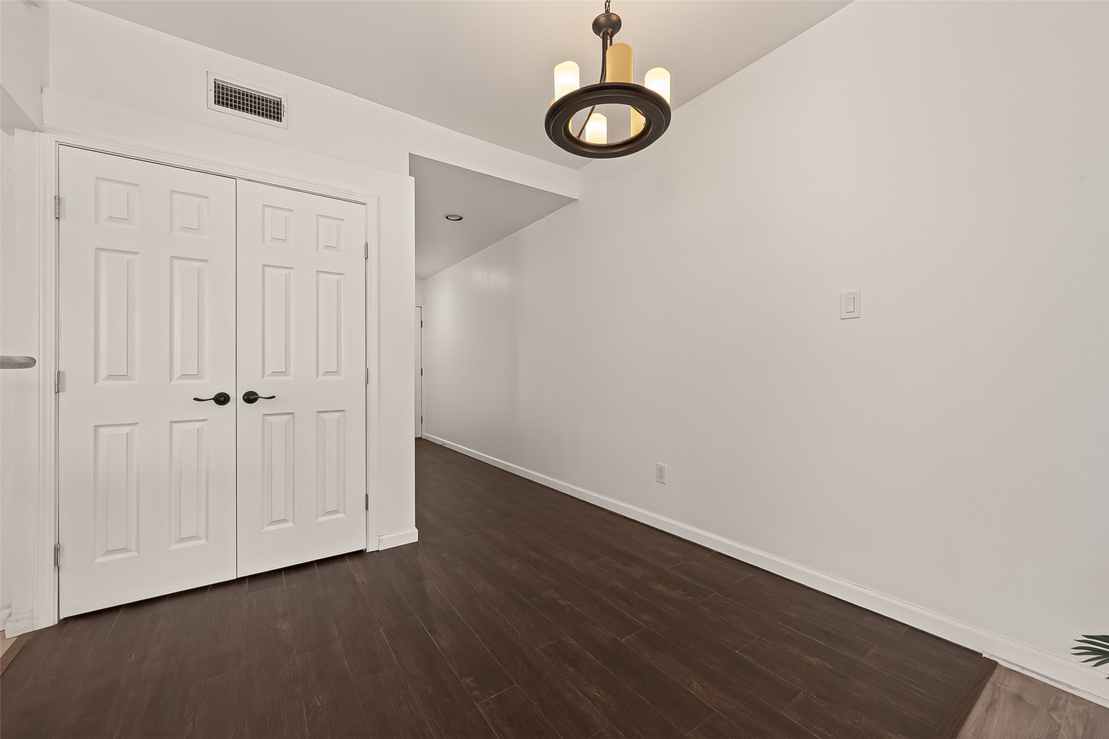 180 April Point Drive South Conroe, TX 77356 - Photo 17 of 39 This photo primary bedroom’s closet a hallway with rich dark wood flooring and white walls. There are double doors with black handles on the left, and a modern ceiling light fixture above. The space is clean and well-lit, suggesting a contemporary and welcoming entryway or corridor.