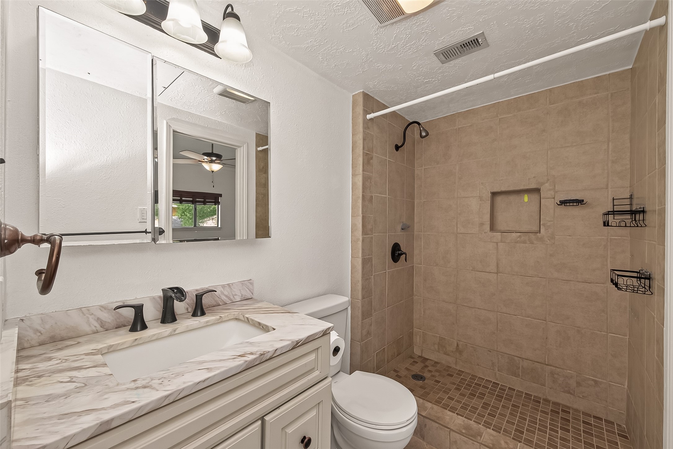 180 April Point Drive South Conroe, TX 77356 - Photo 20 of 39 This bathroom features a modern design with a spacious walk-in shower, beige tile walls, and a built-in shelf. The vanity has a marble countertop with sleek black fixtures and a large mirrored cabinet.