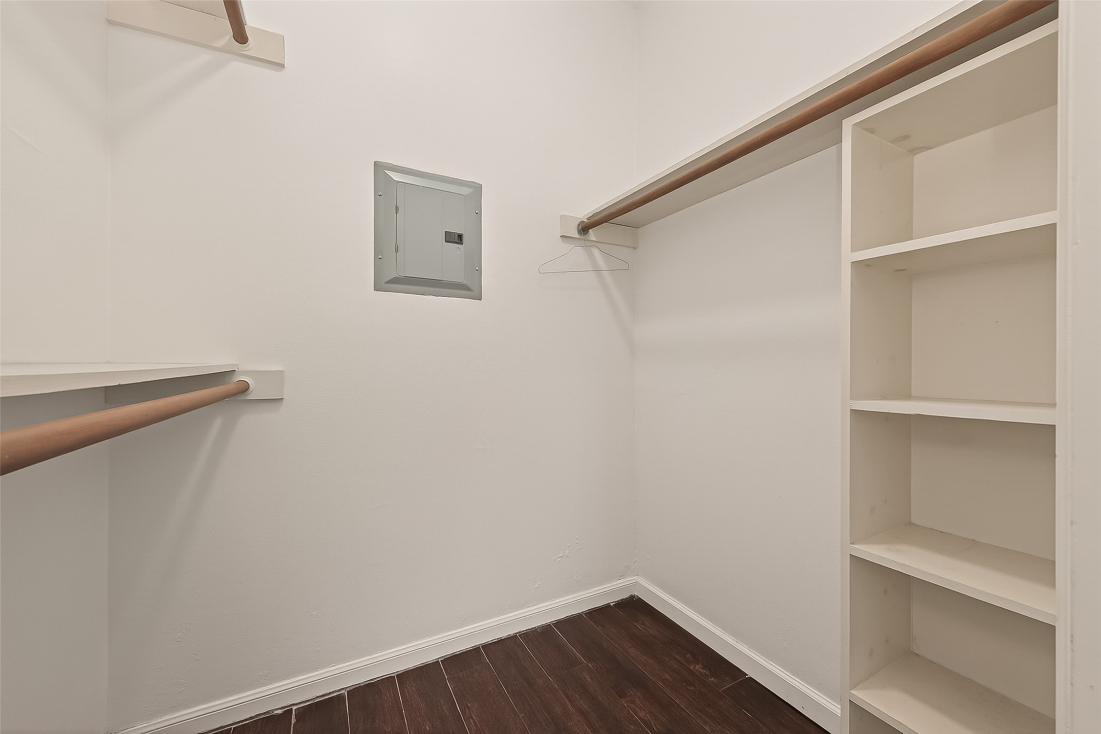 180 April Point Drive South Conroe, TX 77356 - Photo 21 of 39 This photo shows a spacious walk-in closet with dark wood flooring, white walls, multiple wooden hanging rods, and built-in shelving.