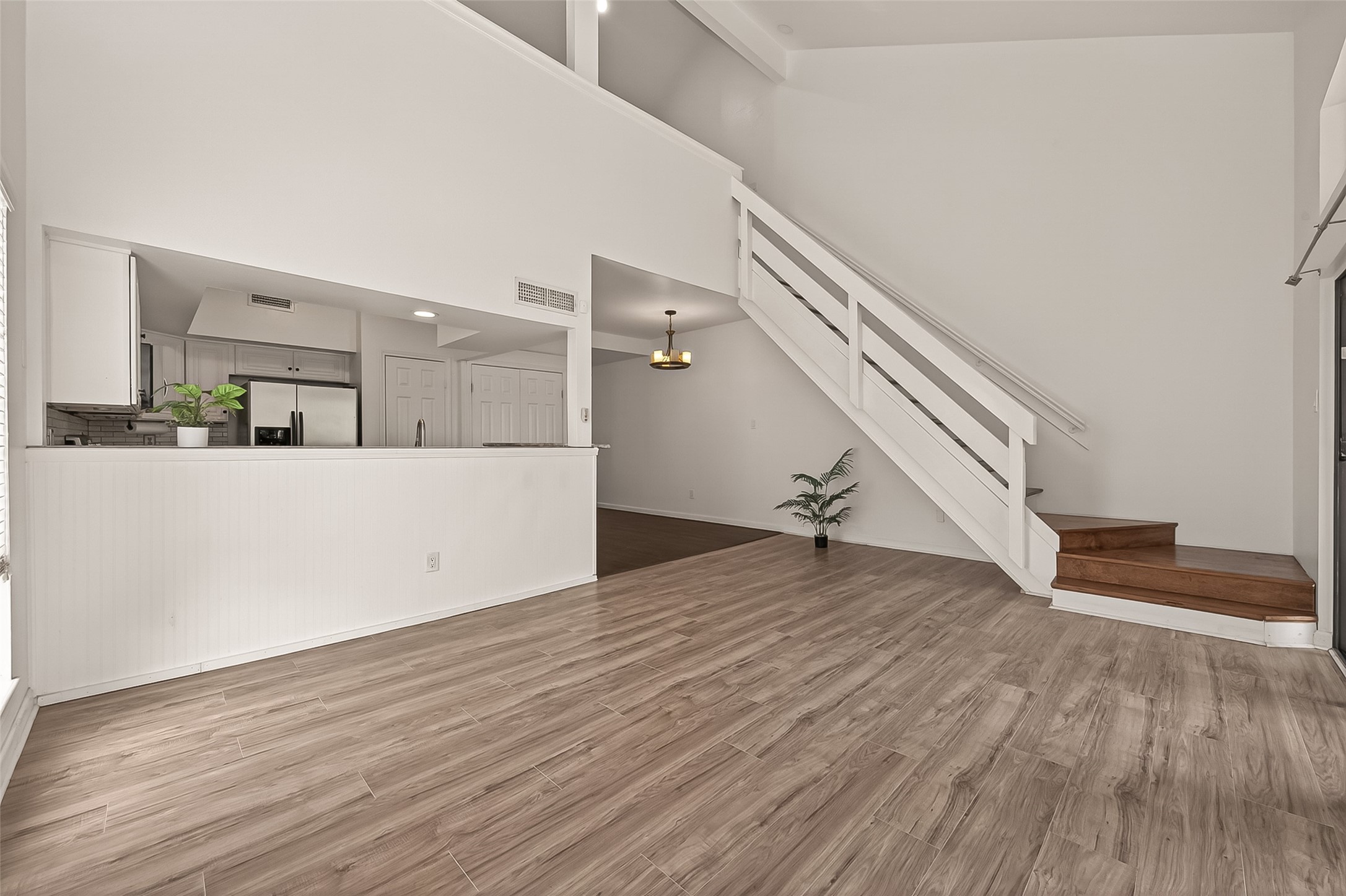 180 April Point Drive South Conroe, TX 77356 - Photo 23 of 39 This photo showcases a modern, open-concept living space with light wood flooring, a sleek staircase, and a partially visible kitchen area featuring stainless steel appliances. The room is bright and airy with high ceilings and neutral walls, ideal for versatile décor.