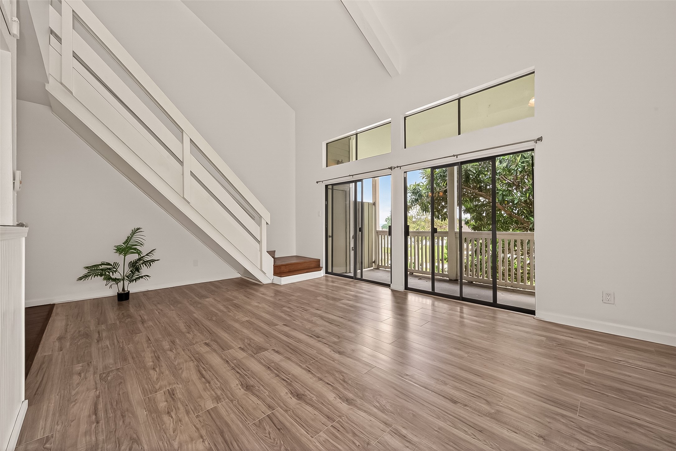 180 April Point Drive South Conroe, TX 77356 - Photo 24 of 39 This photo showcases a bright, open living space with high ceilings, wood-look flooring, and large sliding glass doors leading to a balcony. The modern staircase enhances the spacious, airy feel.