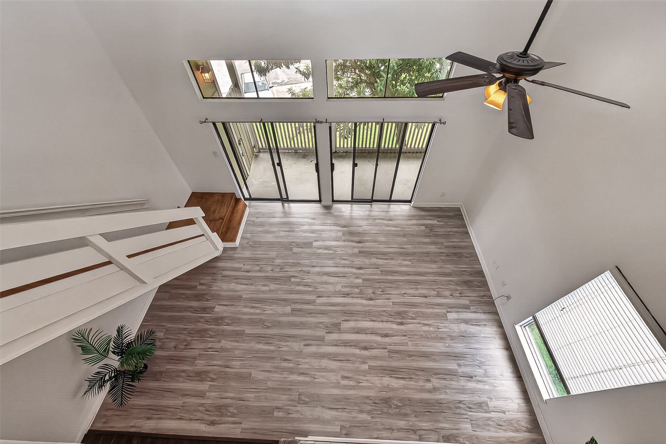 180 April Point Drive South Conroe, TX 77356 - Photo 26 of 39 This photo showcases a spacious, open living area with high ceilings, large windows for natural light, sliding glass doors leading to an outdoor space, and modern wood flooring. A ceiling fan adds comfort, and the overall design is clean and airy.