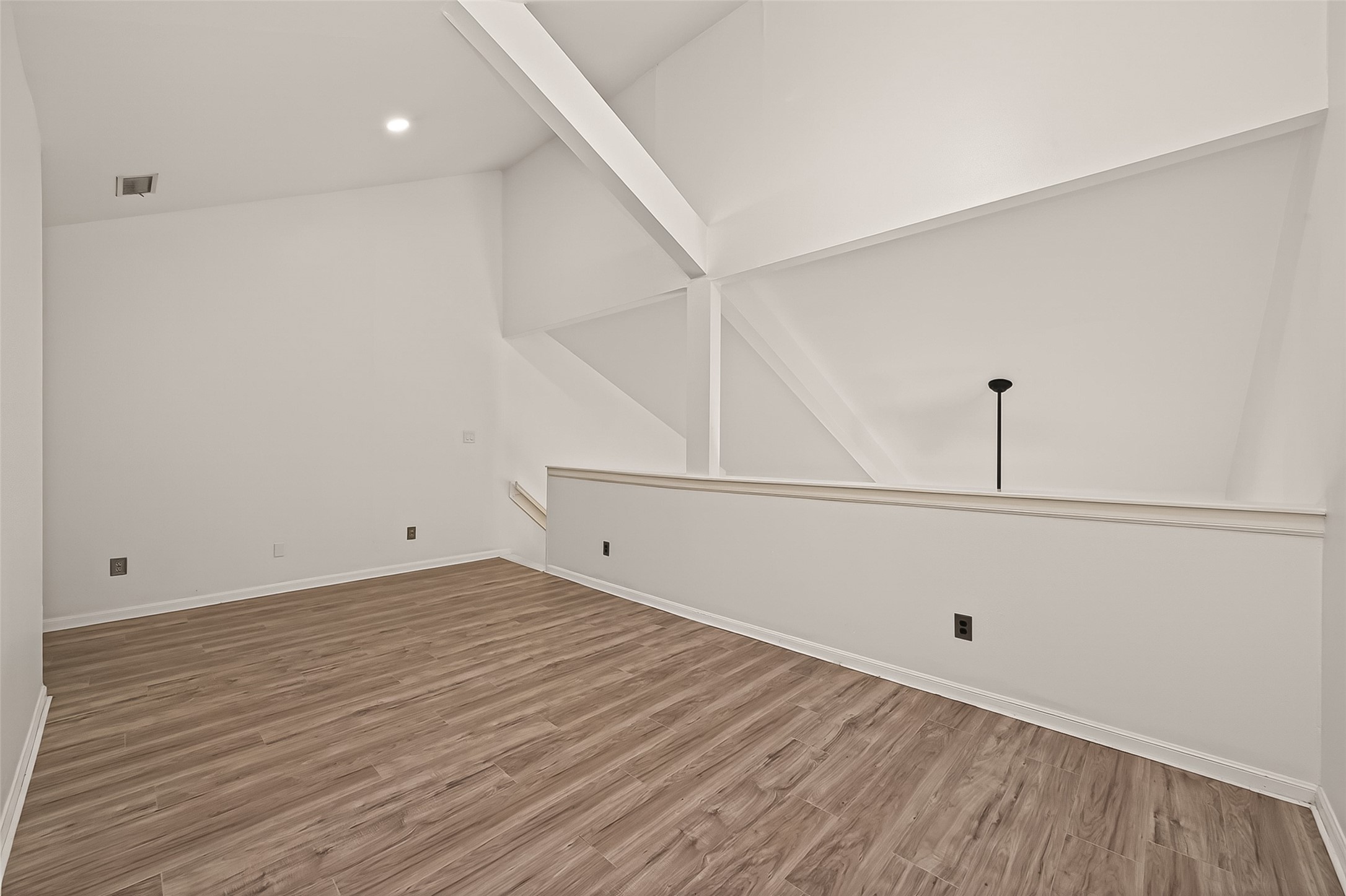 180 April Point Drive South Conroe, TX 77356 - Photo 27 of 39 This photo showcases a bright, open loft space with high ceilings, white walls, and wood-style flooring. The unique architectural beams add character, and the open railing provides a view into the room below, making it perfect for a study or lounge area.