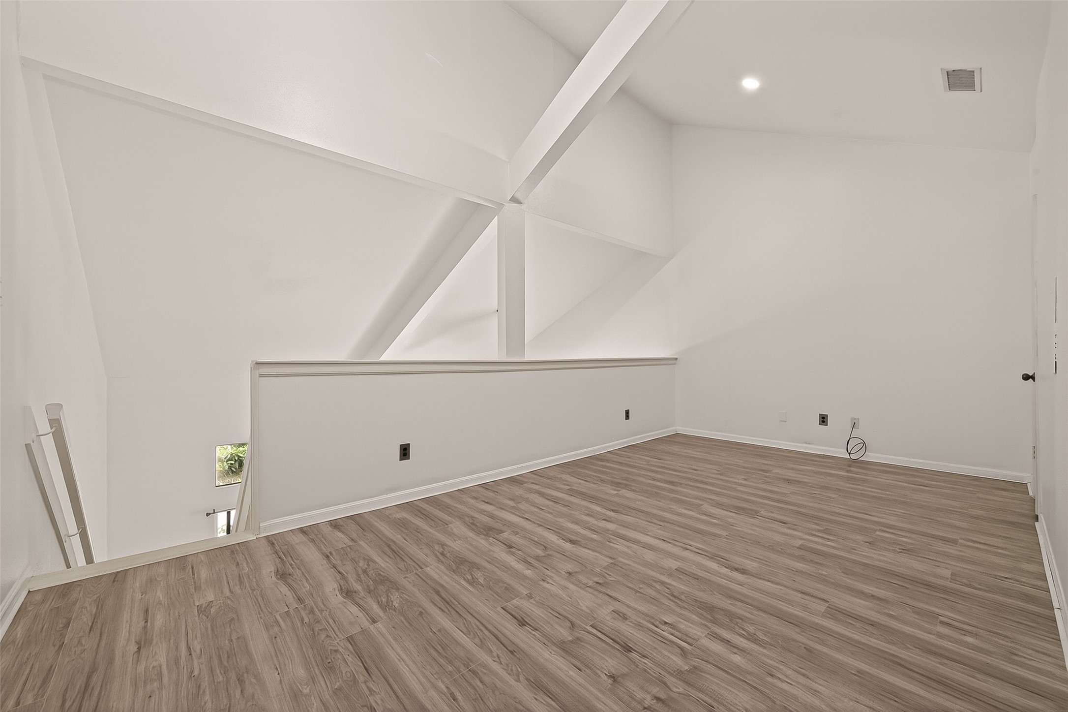 180 April Point Drive South Conroe, TX 77356 - Photo 29 of 39 This photo showcases a spacious, modern loft area with high ceilings and abundant natural light. The room features clean, white walls and sleek wood flooring, offering a versatile space ideal for a home office or entertainment area.