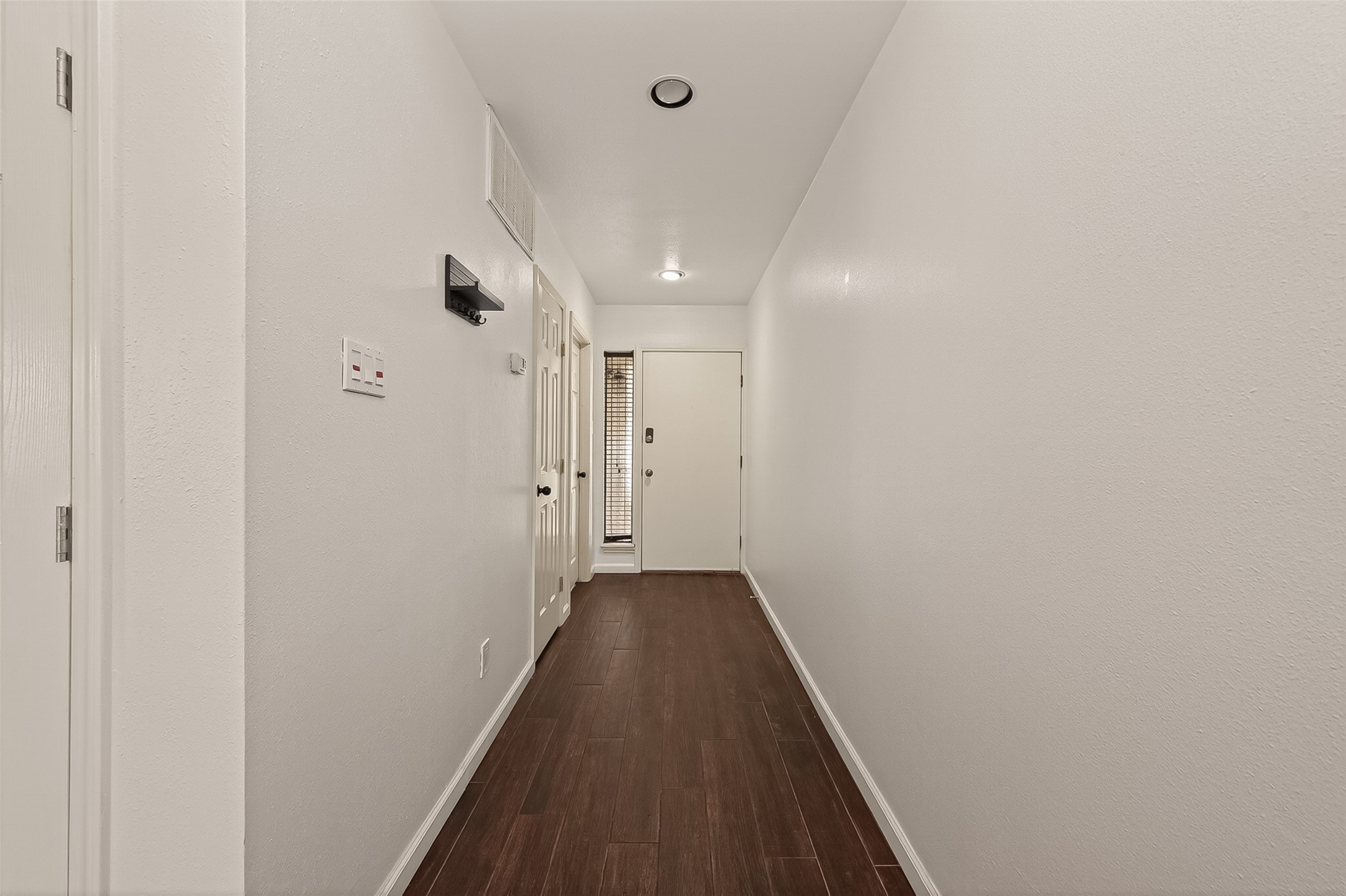 180 April Point Drive South Conroe, TX 77356 - Photo 3 of 39 This photo features a clean, well-lit hallway with dark wood flooring and neutral walls, leading to a door with natural light coming through adjacent blinds.