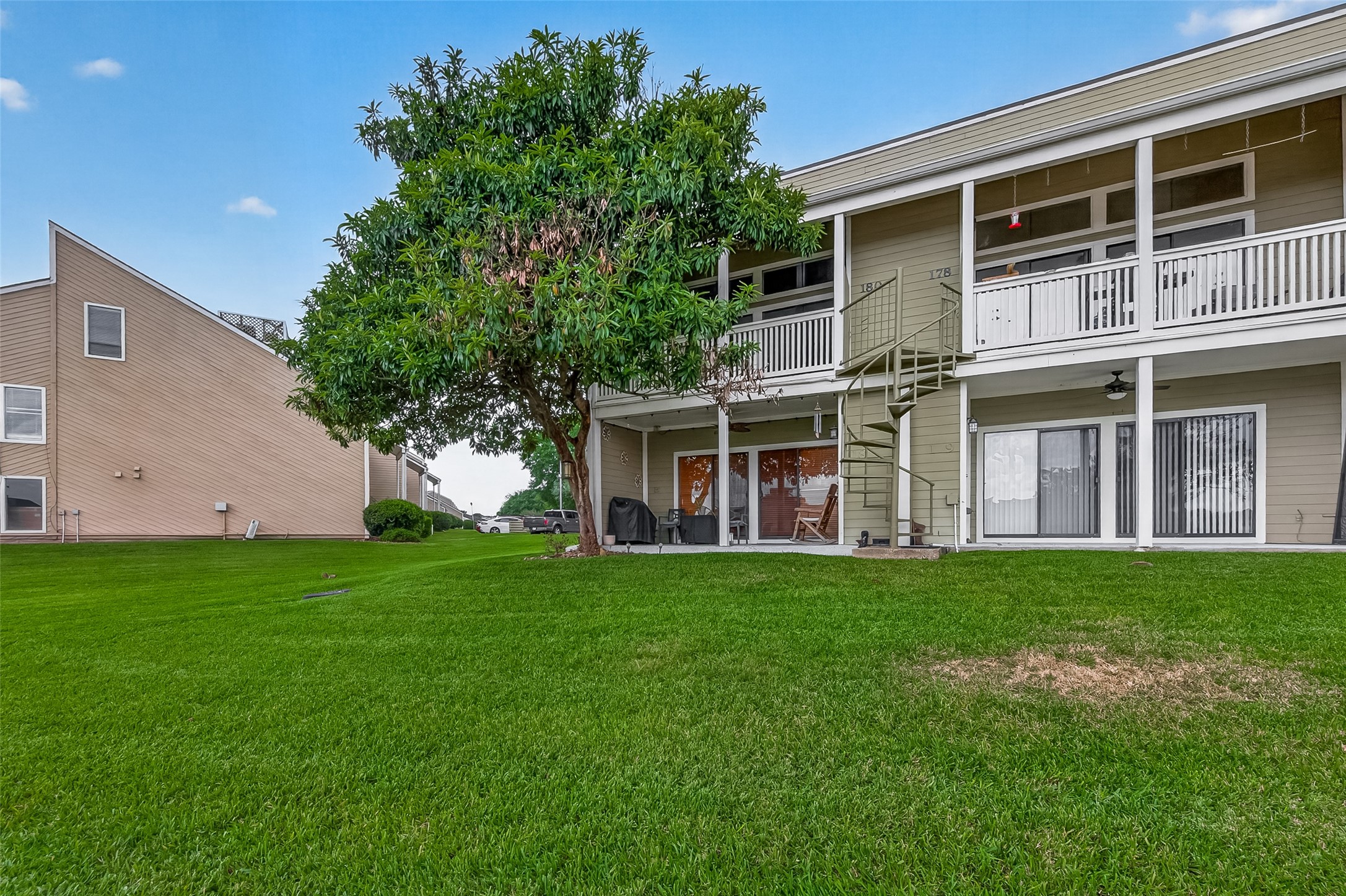 180 April Point Drive South Conroe, TX 77356 - Photo 32 of 39 This photo showcases a two-story home with a spacious lawn, featuring a balcony and a spiral staircase. The exterior is well-maintained with a neutral color palette, and the area is landscaped with mature trees.