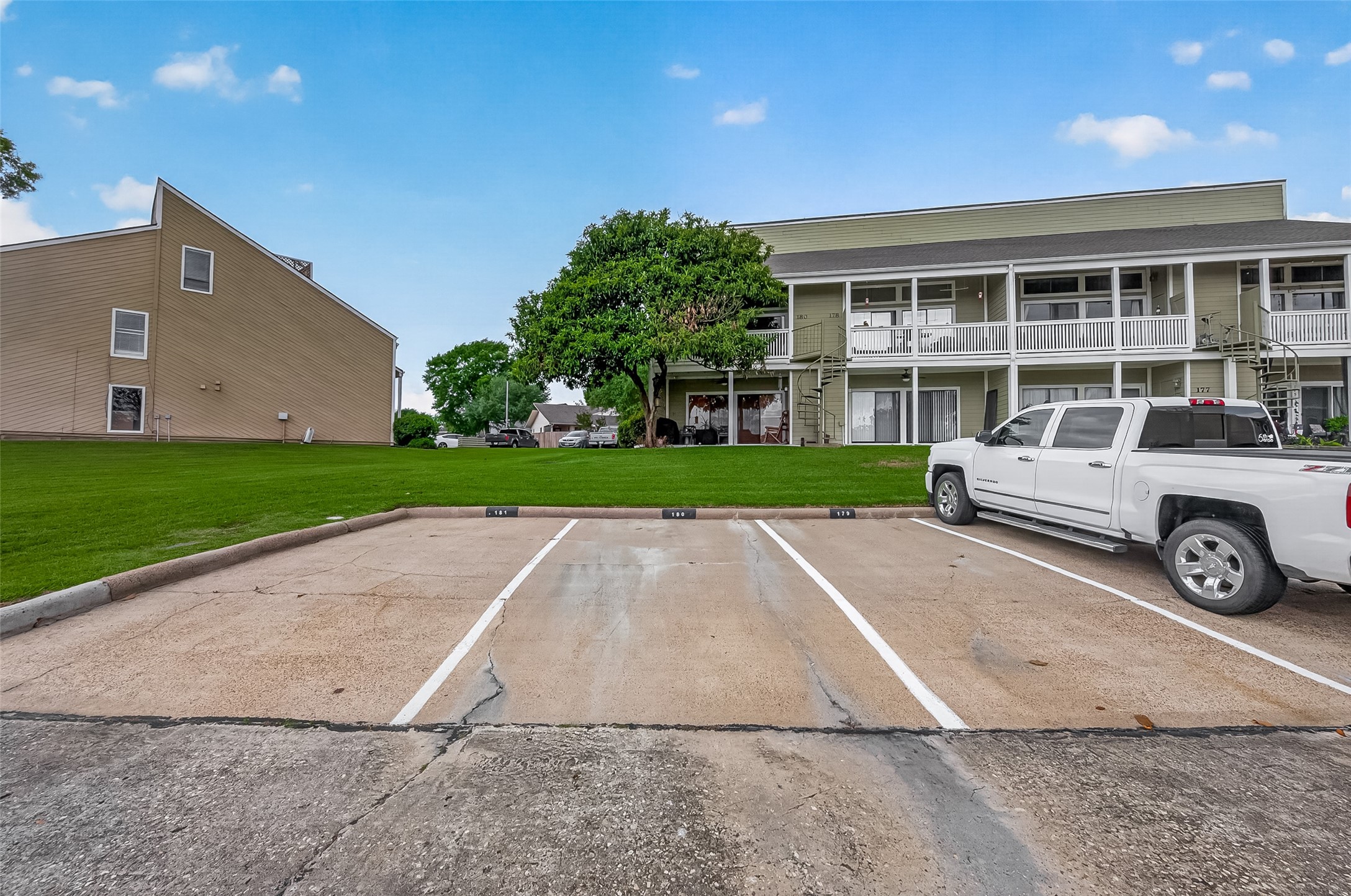 180 April Point Drive South Conroe, TX 77356 - Photo 34 of 39 This photo features a low-rise residential building with a green lawn and ample parking space in front. The building has two levels with balconies and a spiral staircase, creating a welcoming and functional exterior.