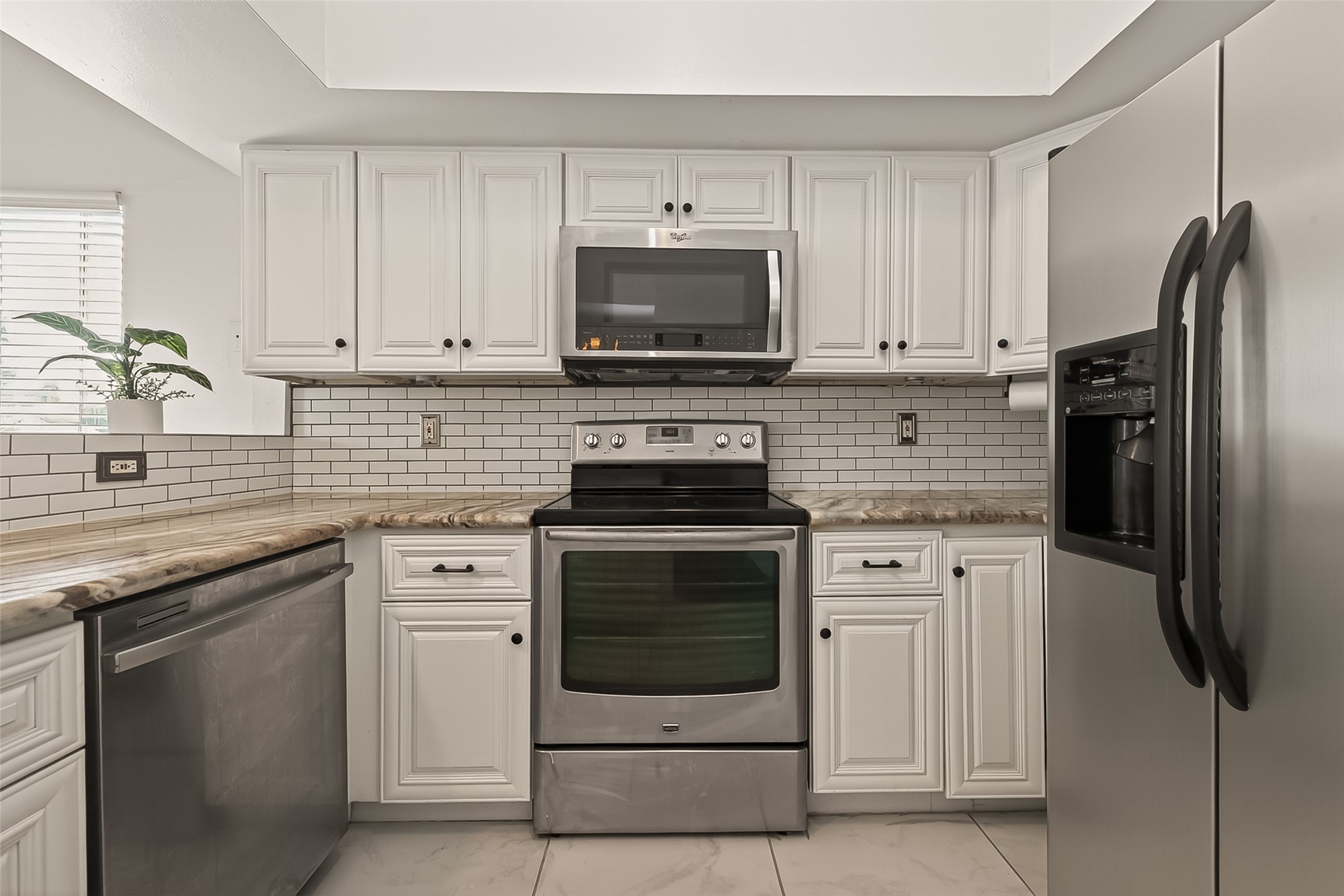180 April Point Drive South Conroe, TX 77356 - Photo 4 of 39 This modern kitchen features sleek stainless steel appliances, white cabinetry, and a stylish subway tile backsplash. The spacious countertops provide ample workspace, and a large window adds natural light.