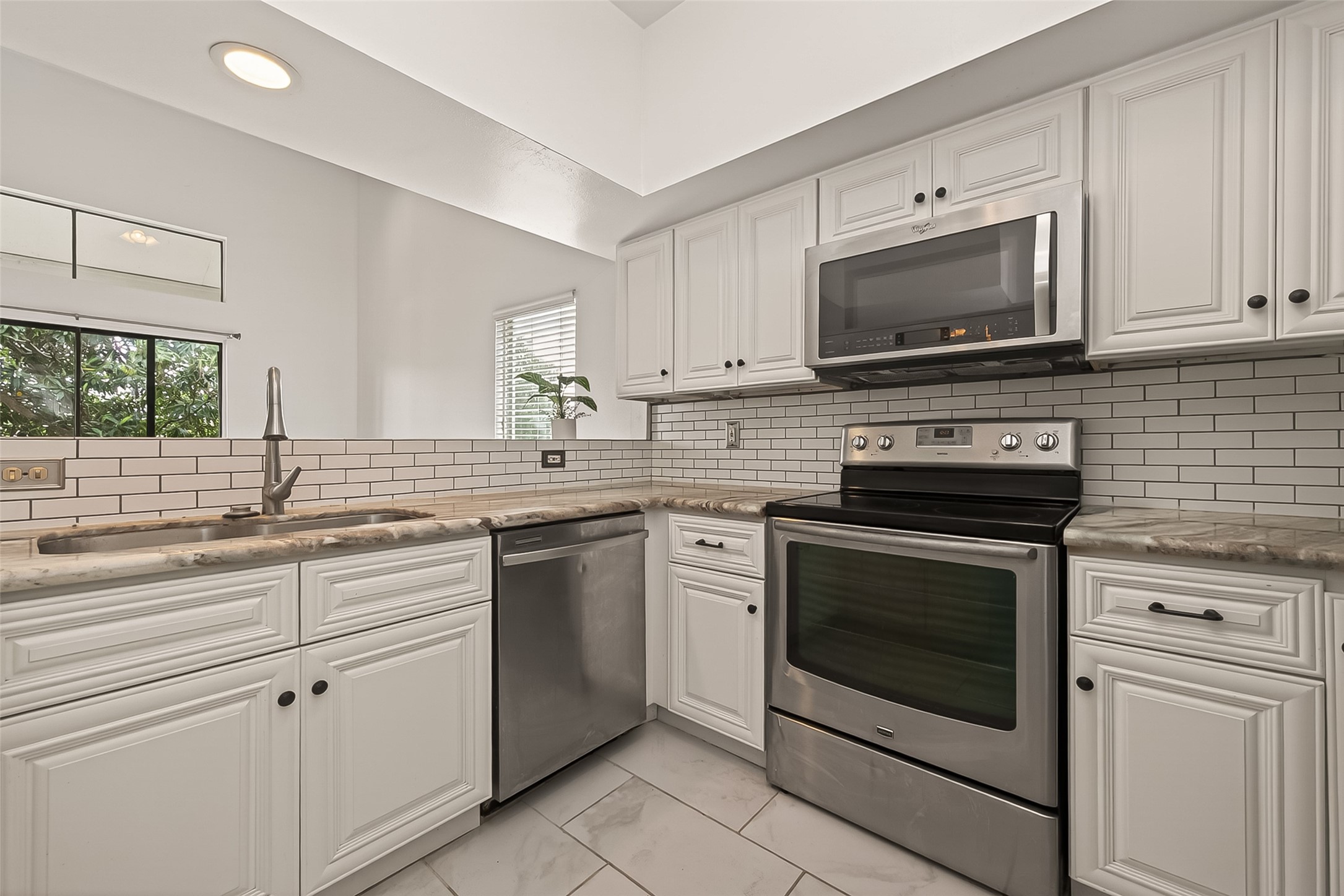 180 April Point Drive South Conroe, TX 77356 - Photo 6 of 39 This modern kitchen features sleek stainless steel appliances, white cabinetry, and a stylish subway tile backsplash. The space is bright and inviting, with ample natural light and elegant marble countertops.