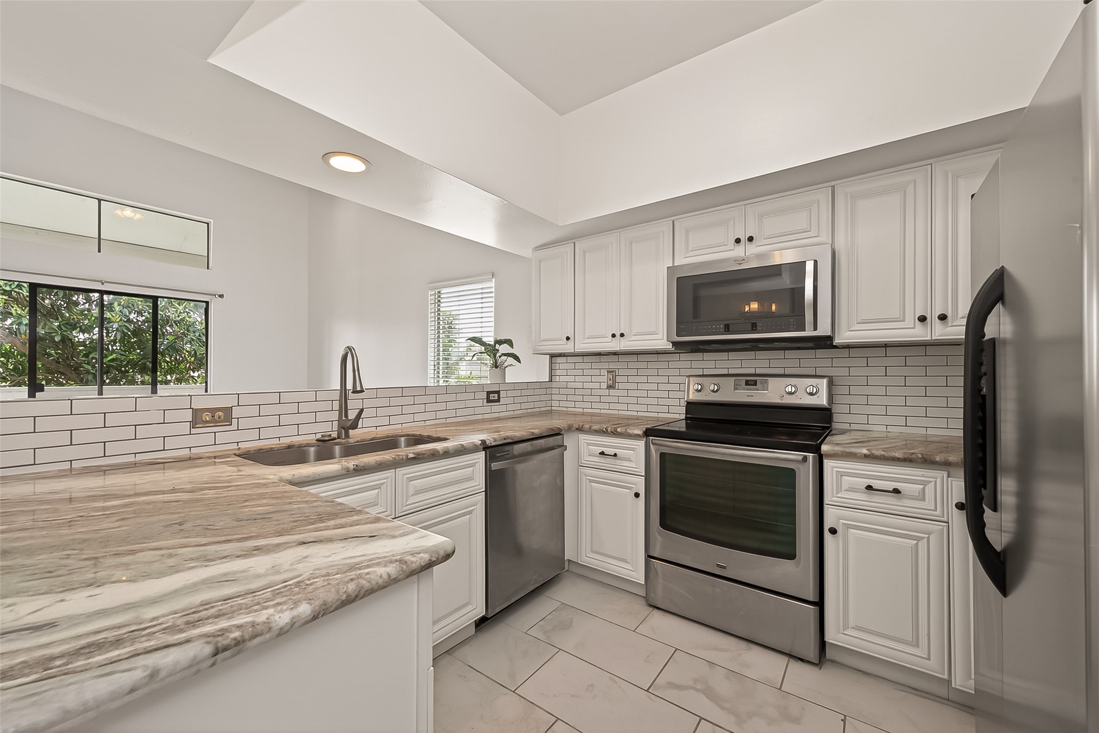 180 April Point Drive South Conroe, TX 77356 - Photo 7 of 39 This modern kitchen features sleek stainless steel appliances, white cabinetry, and a stylish subway tile backsplash. The marble countertops add a touch of elegance, and large windows provide ample natural light.