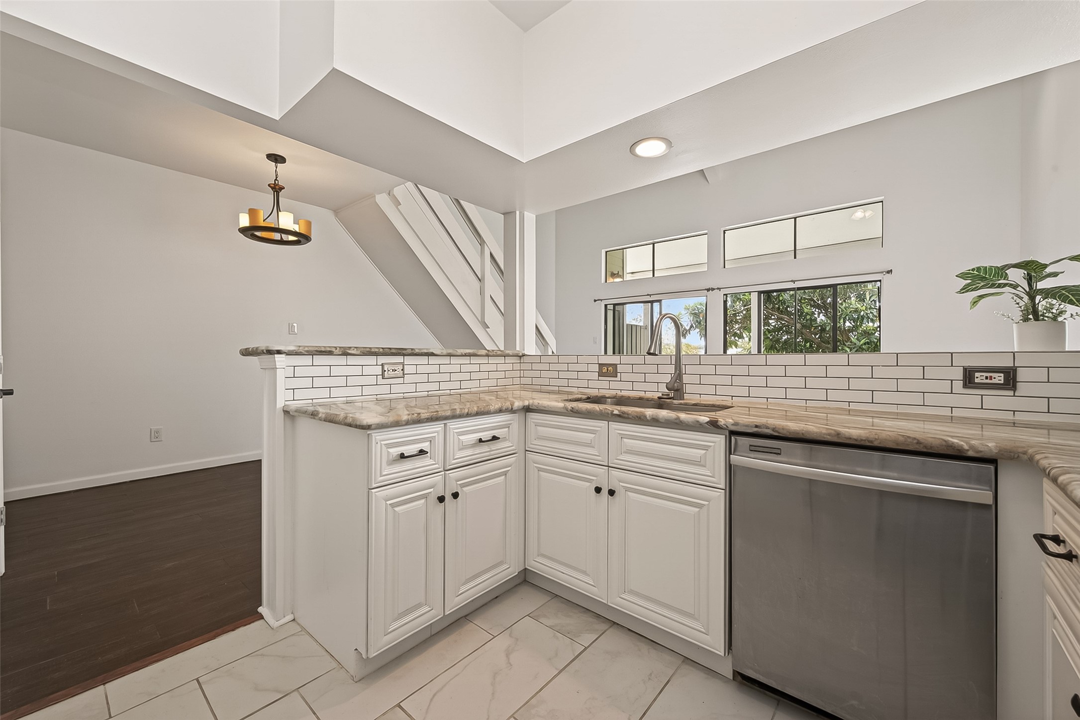 180 April Point Drive South Conroe, TX 77356 - Photo 8 of 39 This modern kitchen features white cabinetry, granite countertops, and a sleek subway tile backsplash. It includes stainless steel appliances, ample natural light from large windows, and a stylish pendant light over the open layout.