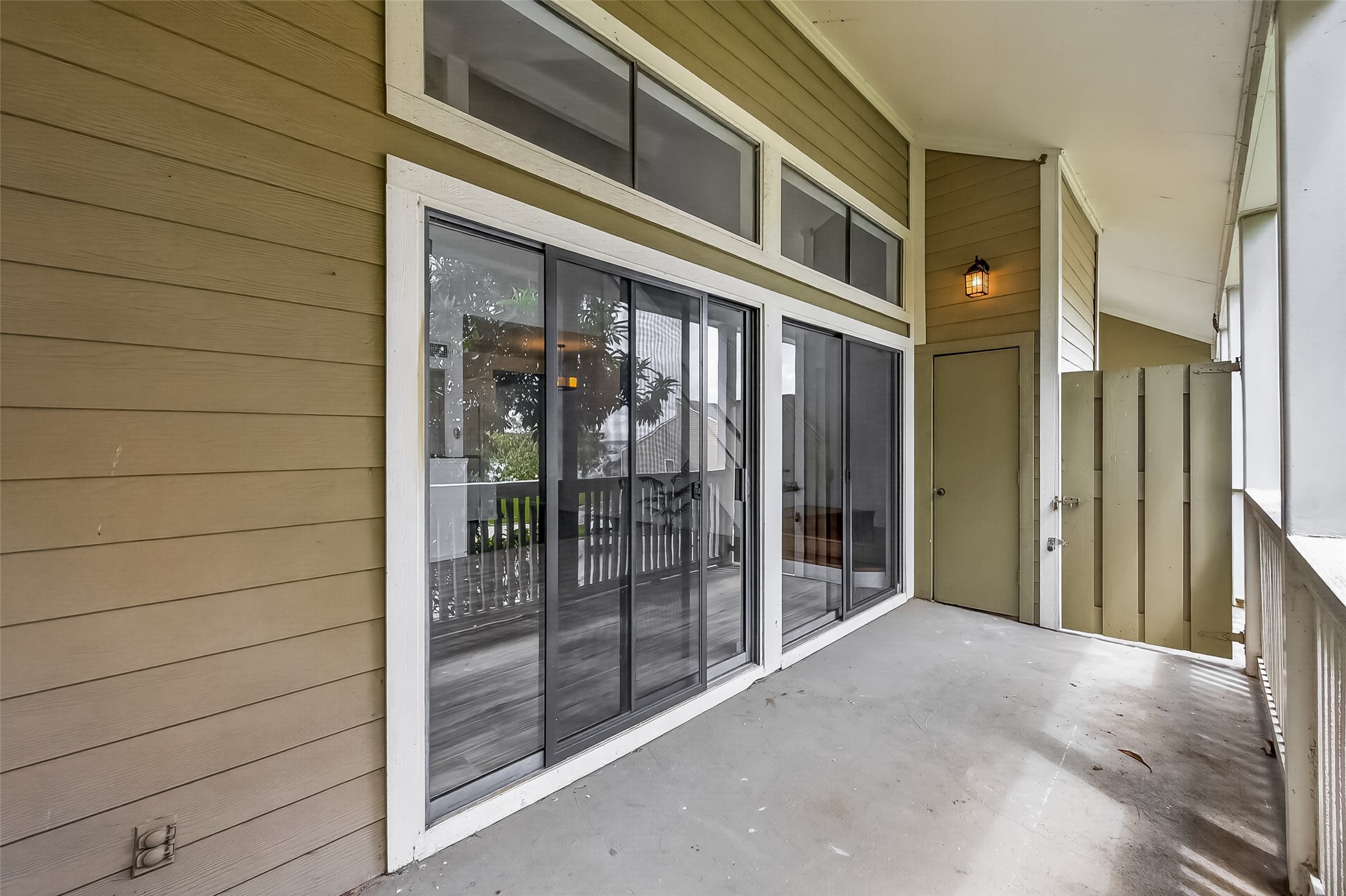 180 April Point Drive South Conroe, TX 77356 - Photo 10 of 39 This photo shows a covered balcony with sliding glass doors, providing access to the indoor living area. The space features a high ceiling, wood siding, and a wall light fixture, offering a cozy outdoor extension for relaxation or entertaining.