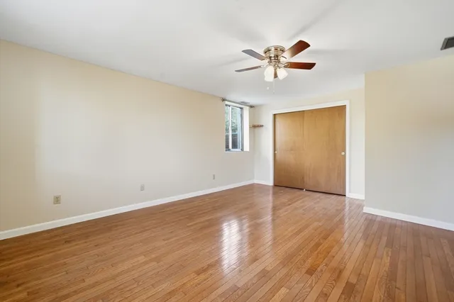 a view of an empty room with wooden floor and a ceiling fan