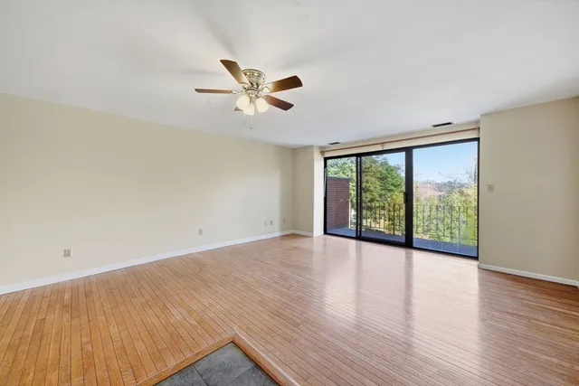 an empty room with wooden floor fan and windows