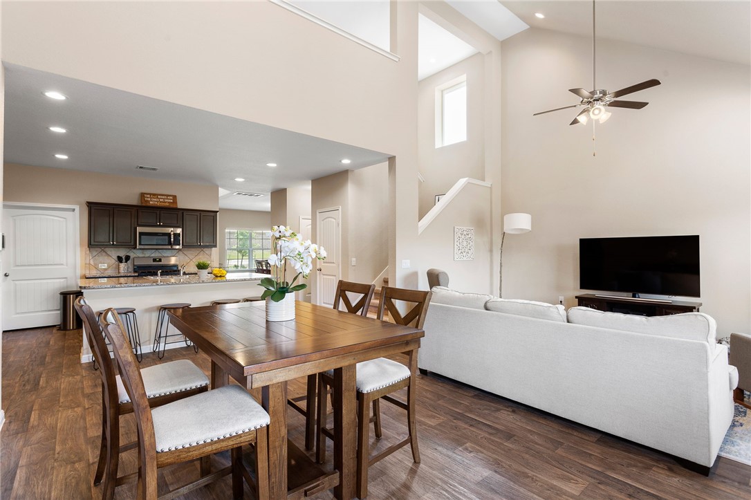 a living room with stainless steel appliances a dining table wooden floor and a kitchen view