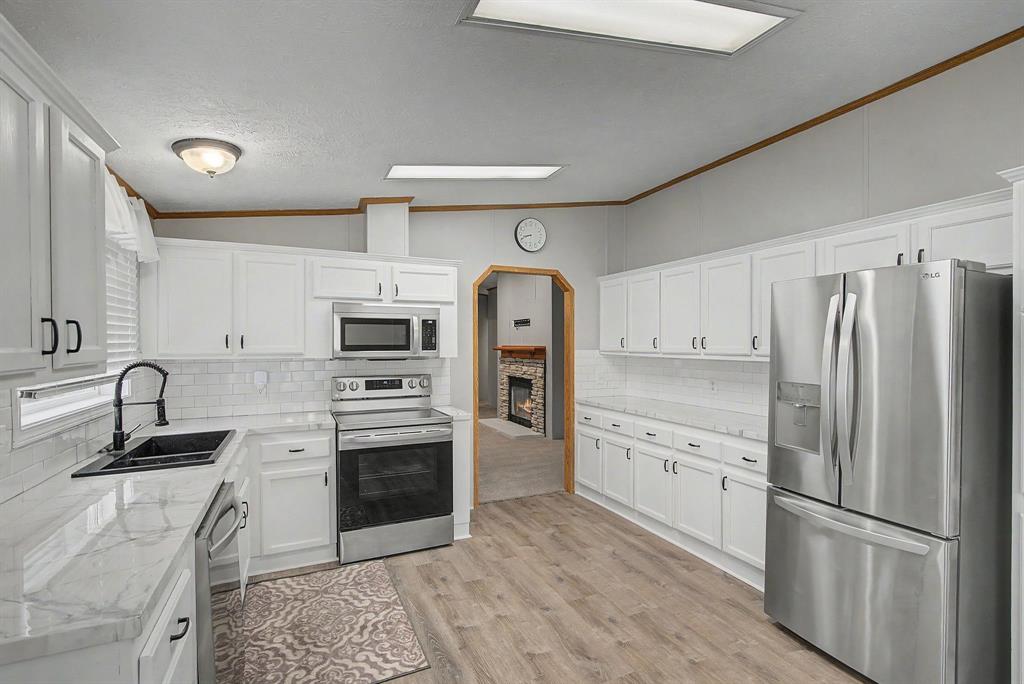 1202 Princeton Road Princeton, LA 71067 - Photo 7 of 19 Kitchen featuring white cabinetry, wood-finish flooring, stainless steel appliances, a white subway tile backsplash, and light-toned countertops