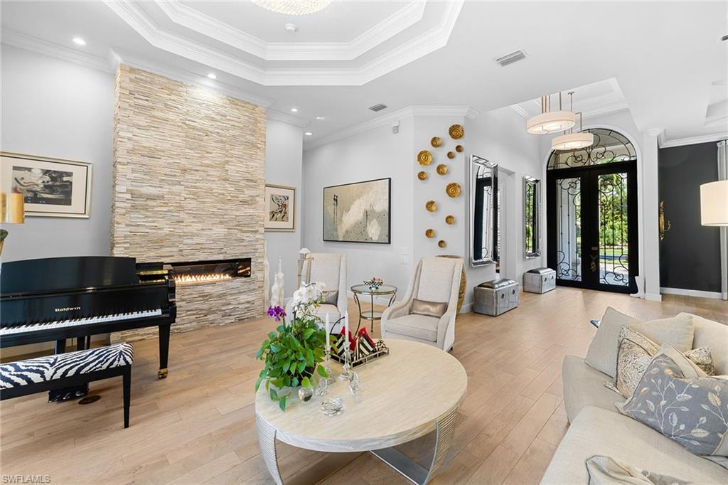7837 Classics Drive Naples, FL 34113 - Photo 10 of 50 Living area featuring french doors, a large fireplace, ornamental molding, hardwood / wood-style floors, and a raised ceiling