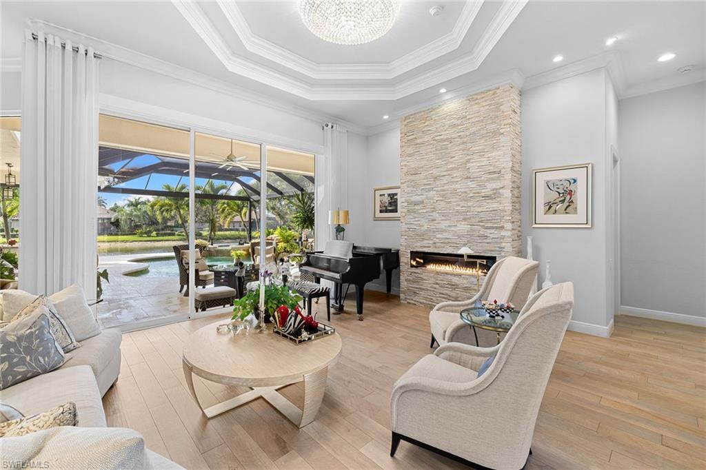 7837 Classics Drive Naples, FL 34113 - Photo 13 of 50 Living room featuring a sunroom, light wood-style floors, a fireplace, a raised ceiling, and crown molding