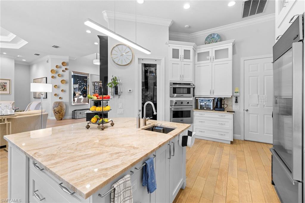7837 Classics Drive Naples, FL 34113 - Photo 49 of 50 Kitchen with crown molding, white cabinetry, stainless steel appliances, open floor plan, and light wood-style flooring