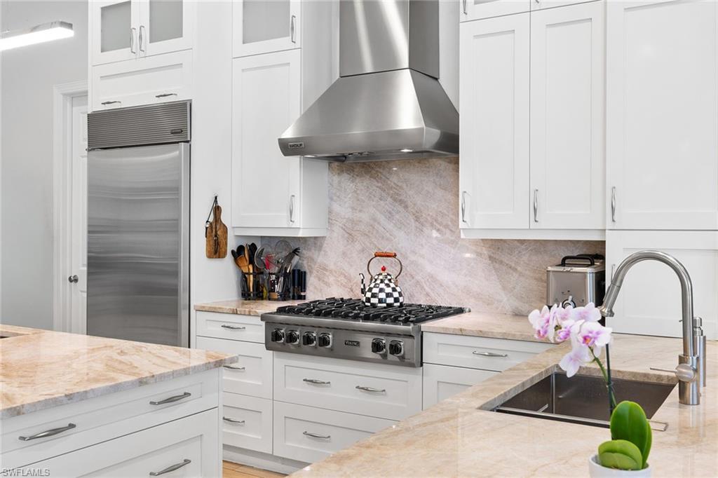 7837 Classics Drive Naples, FL 34113 - Photo 18 of 50 Kitchen with wall chimney range hood, decorative backsplash, white cabinets, and stainless steel appliances