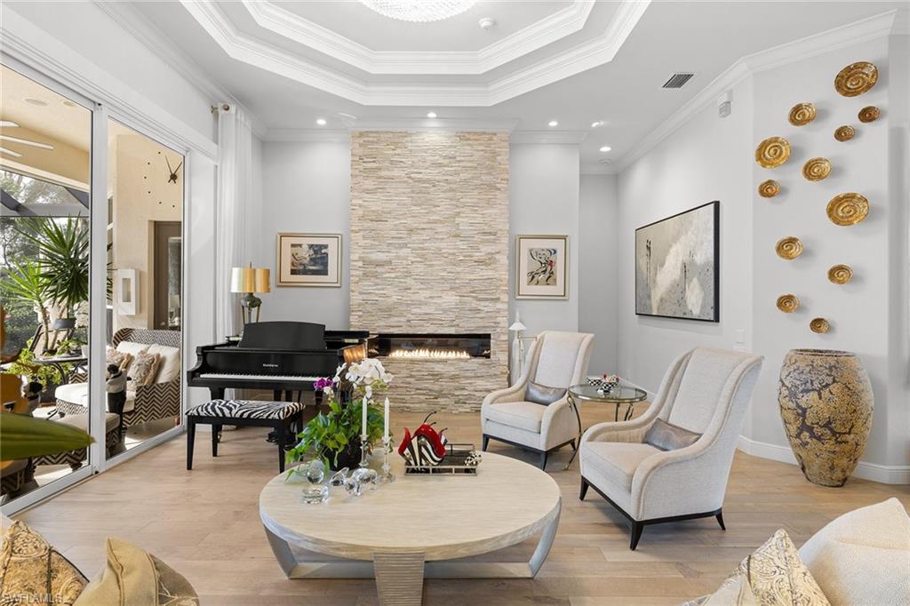 7837 Classics Drive Naples, FL 34113 - Photo 20 of 50 Living area featuring wood finished floors, ornamental molding, a tiled fireplace, and a raised ceiling