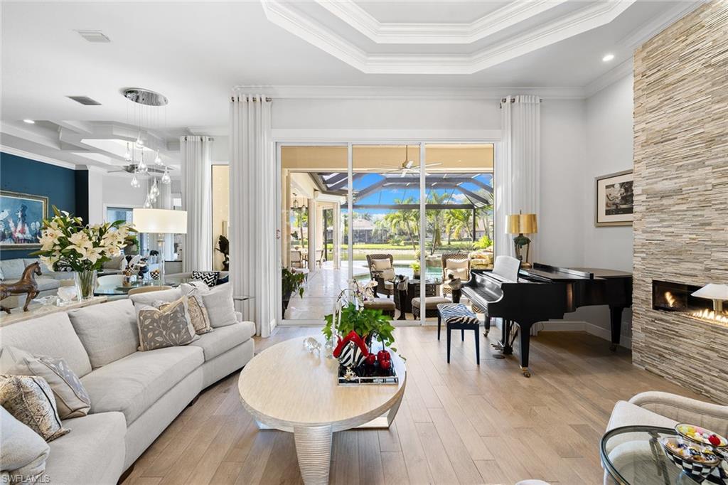 7837 Classics Drive Naples, FL 34113 - Photo 7 of 50 Living area featuring a tray ceiling, a sunroom, a fireplace, hardwood / wood-style floors, and crown molding