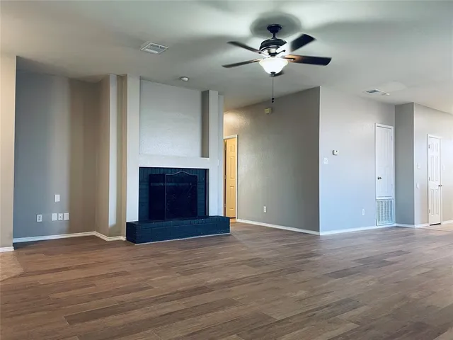 a view of an empty room with wooden floor and a ceiling fan