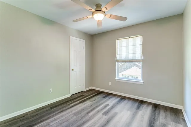 an empty room with wooden floor chandelier fan and windows
