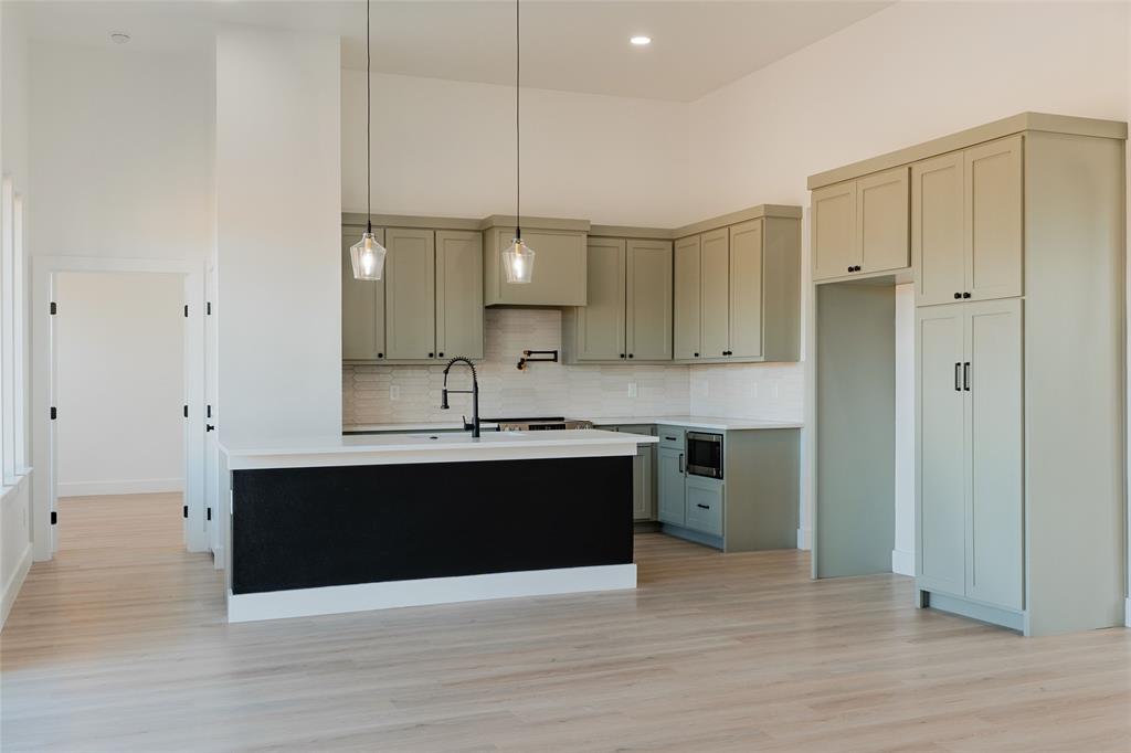 592 Highview Court Godley, TX 76044 - Photo 3 of 21 Kitchen with a high ceiling, pendant lighting, light wood-style flooring, a kitchen island with sink, and stainless steel microwave