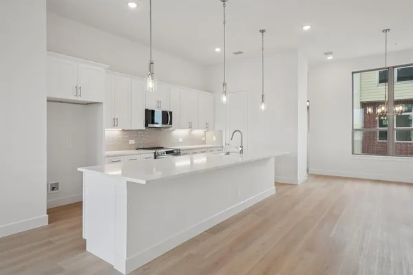 a kitchen with stainless steel appliances granite countertop a sink a microwave oven a refrigerator and white cabinets with wooden floor